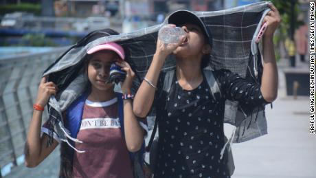 الفتيات يغطين رؤوسهن بينما يمشين ويشربن الماء في حرارة بعد الظهر الحارقة في مومباي.